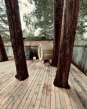 Cedar barrel sauna on a wide wooden deck built around towering tree trunks