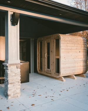 Cedar cabin sauna with three glass front panels under a covered patio in warm autumn light