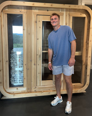 Smiling man standing in front of an indoor cedar cabin sauna with three glass panels