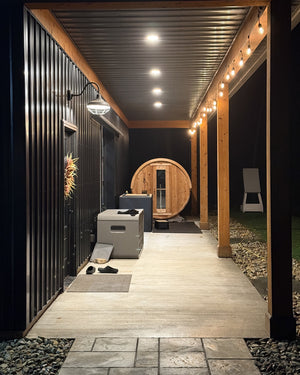 Cedar barrel sauna glowing at the end of a covered walkway lit by string lights and ceiling lights at night