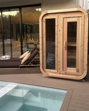 Cedar cabin sauna with glass panels and a glowing heater, beside a small pool and lounge chairs at a modern home