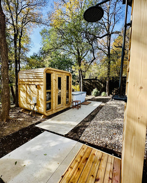 Cedar cabin sauna with three glass front panels beside a white cold plunge, seen from a cedar outdoor shower