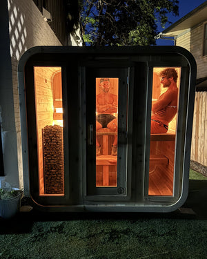 Cabin sauna glowing warm orange at night with two people relaxing inside, seen through three glass panels