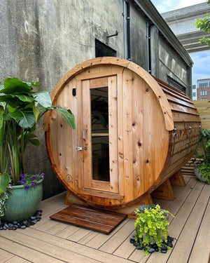 Cedar barrel sauna on a composite deck framed by tropical plants against a concrete wall