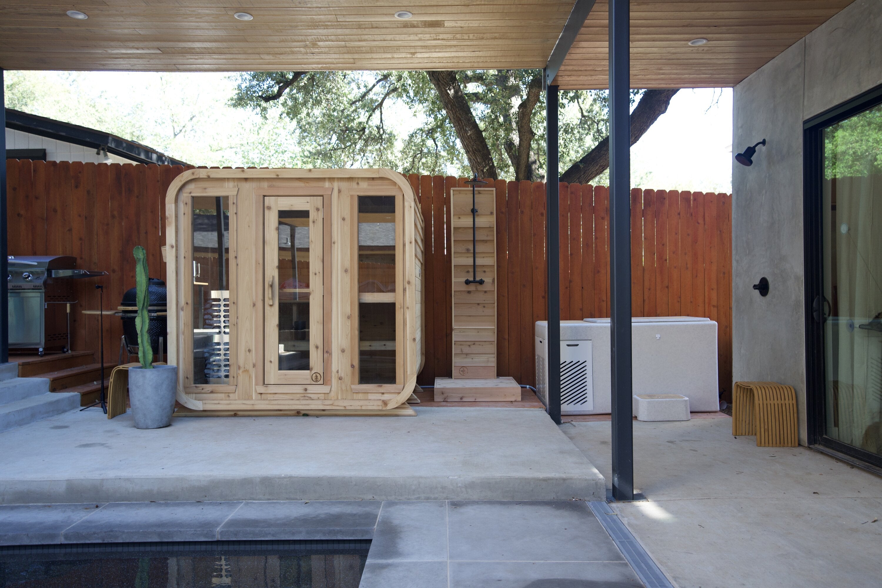 Cedar cabin sauna with three glass panels, an outdoor shower and a cold plunge on a covered poolside patio