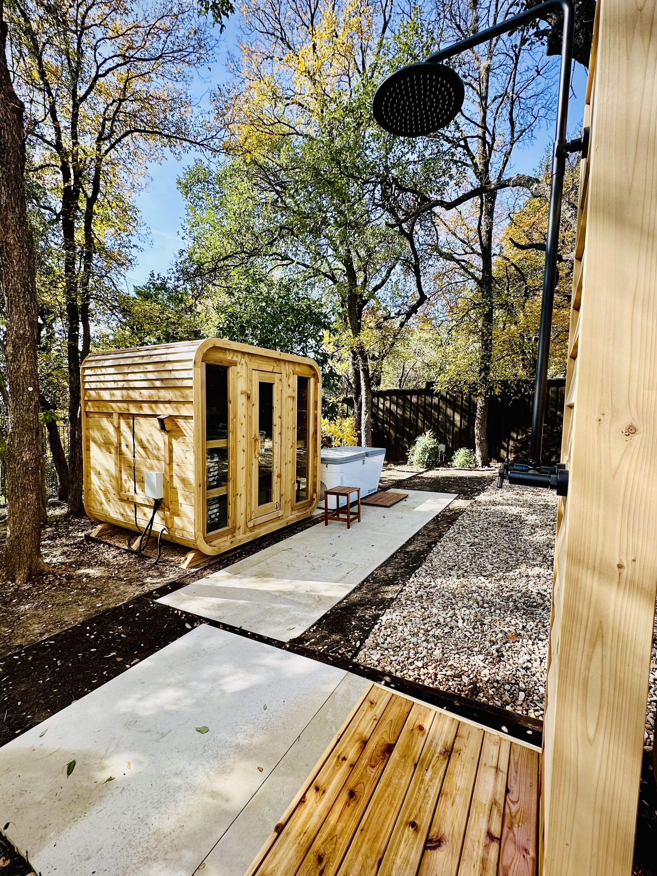 Cedar cabin sauna with three glass front panels beside a white cold plunge, seen from a cedar outdoor shower